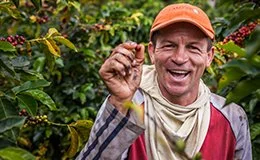 Man in a coffee bean field showing a coffee bean to the camera