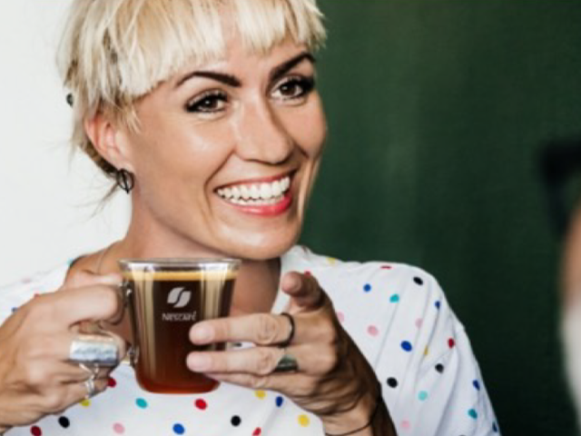 female smiling and holding a glass cup of Nescafe coffee