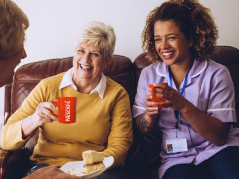 two older females sitting laughing and drinking coffee with a nurse