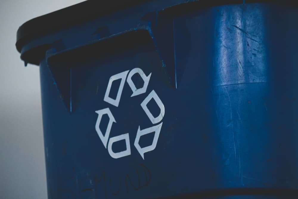 Close-up of a worn blue recycling bin with the recycling symbol prominently displayed on its side.