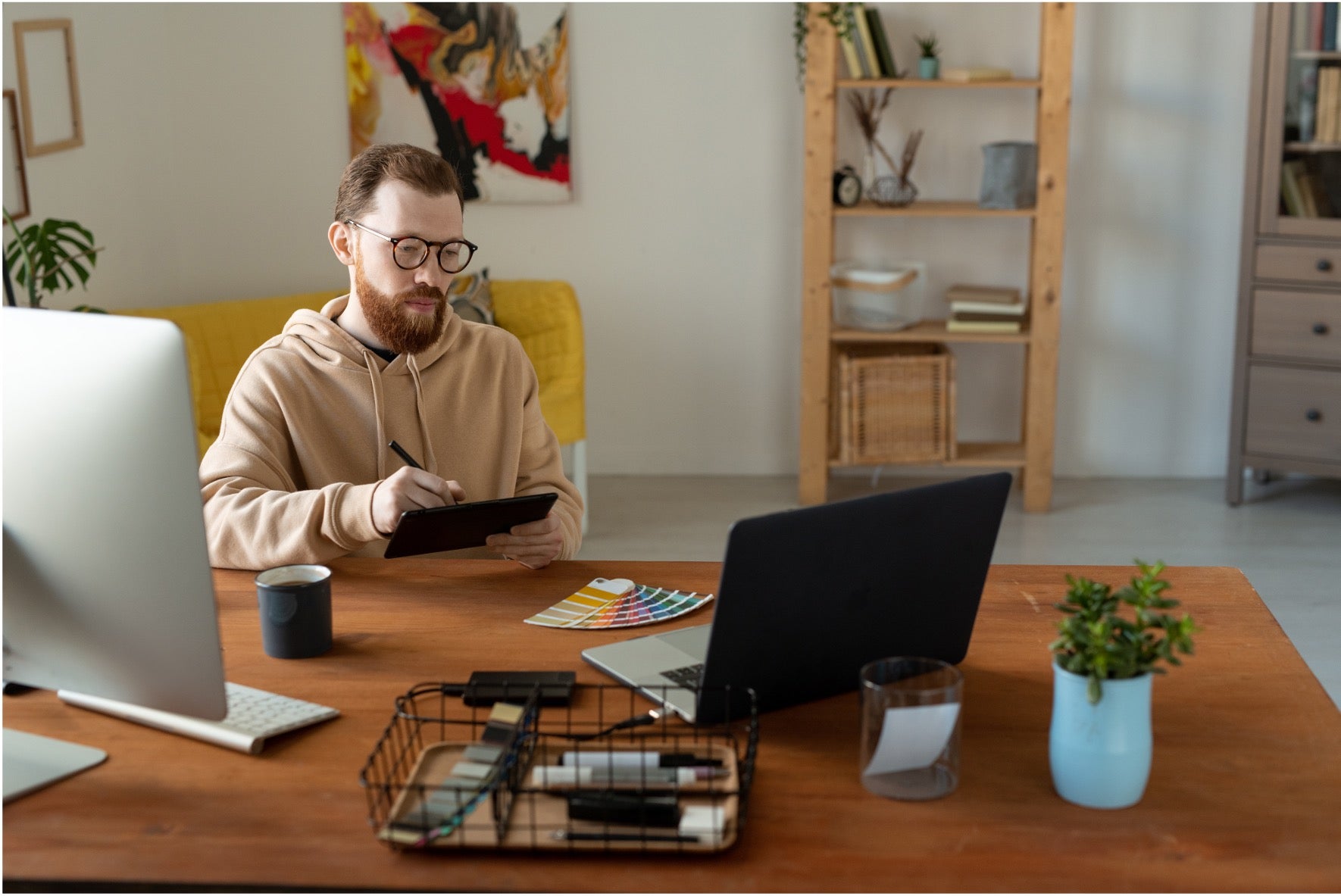 A man sat at his desk at home looking at his laptop and computer screen.