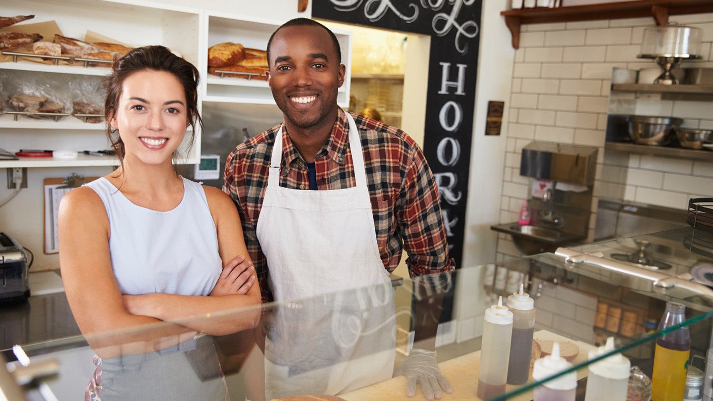 a male and female small business owners behind a bakery counter, smiling