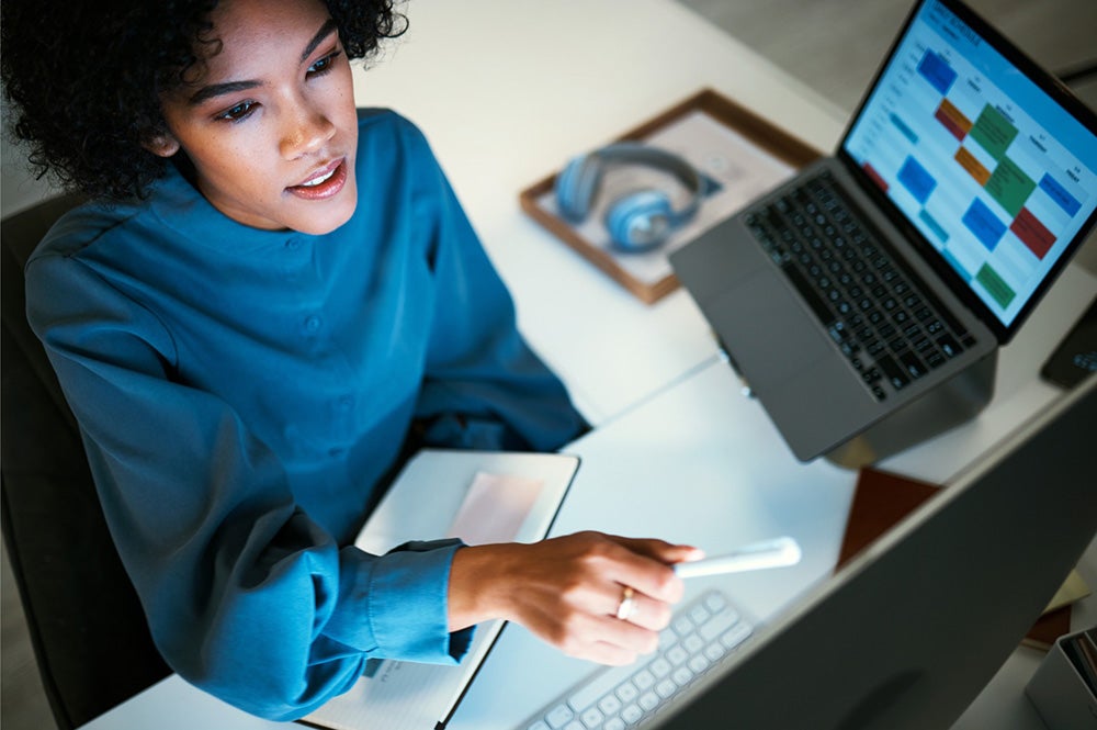 woman pointing at her computer screen whilst holding a clipboard