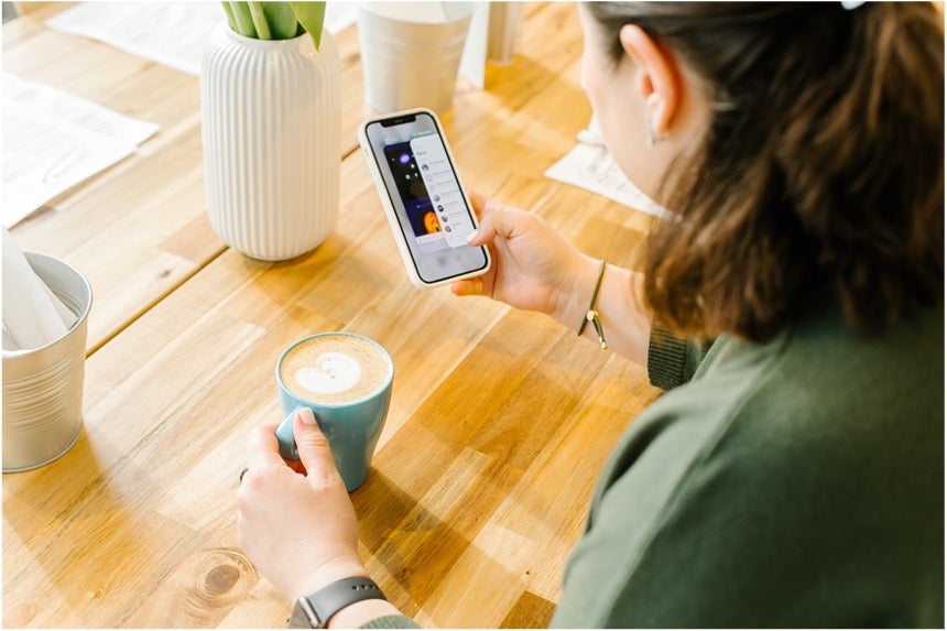 A woman holding her coffee while working form her phone, using a productivity app.