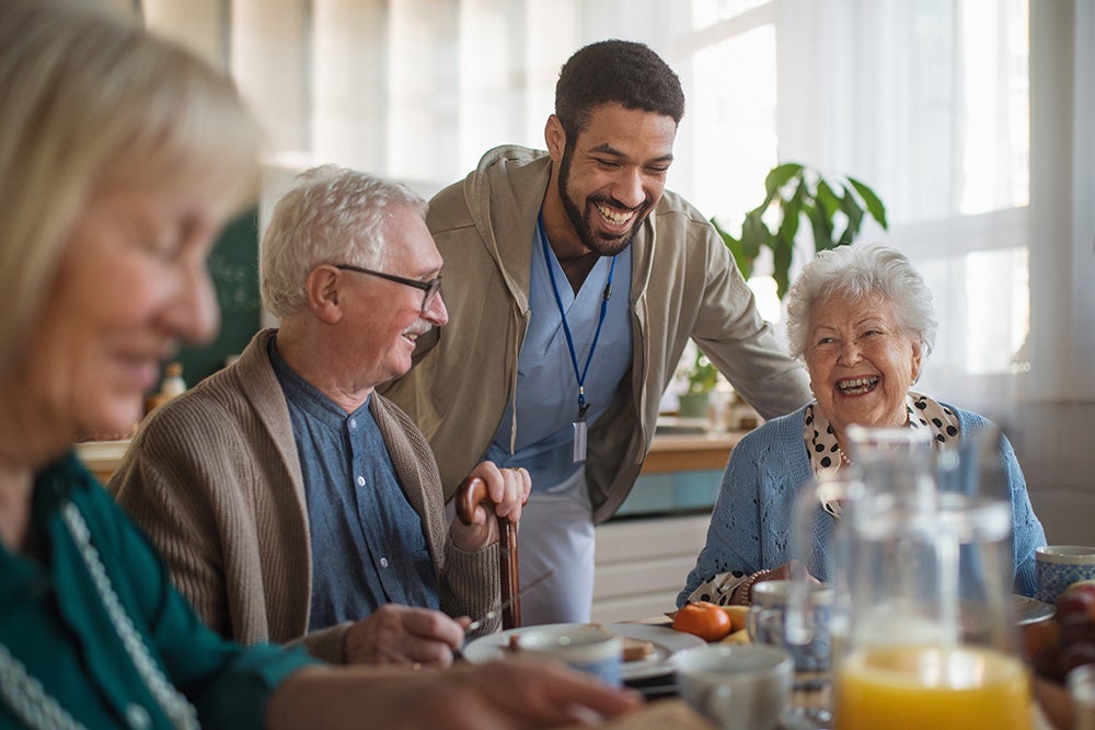 elderly-care-home-staff-around-table-laughing-eating
