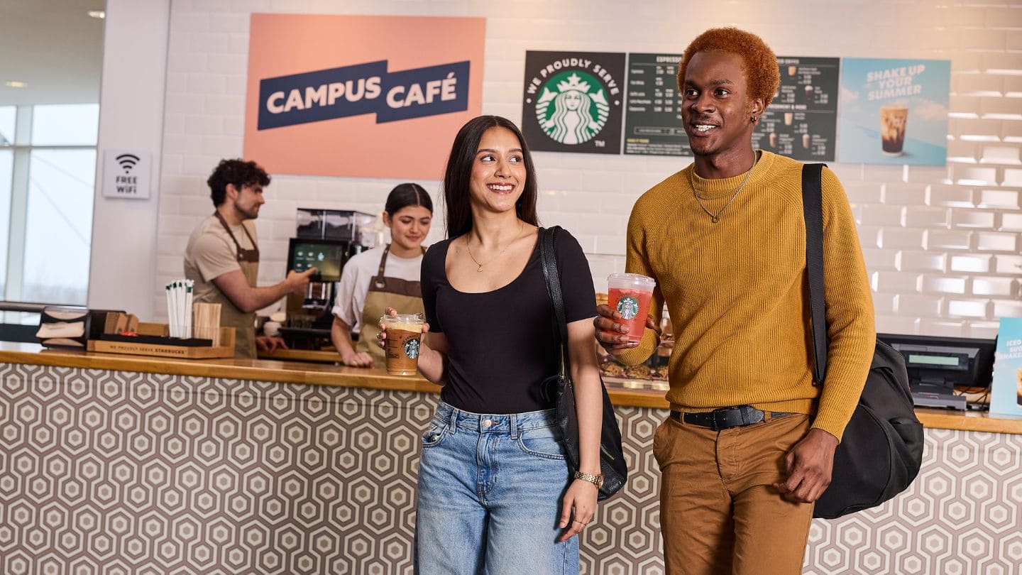 two students holding coffee cups at university cafe