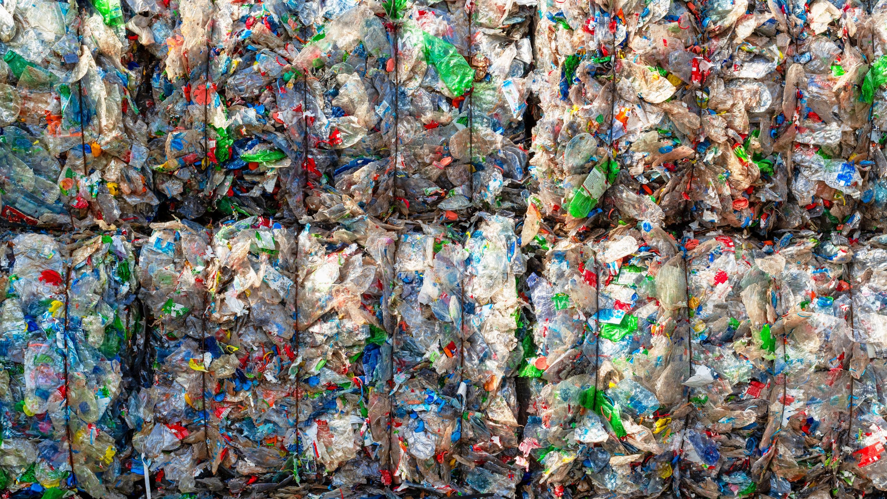 A close-up of compacted plastic waste, showing a colorful mix of crumpled bottles and wrappers, highlighting recycling