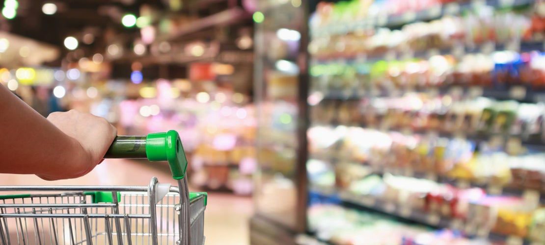 Hand holding trolley at supermarket with blurred view of the shelves full of packaged products
