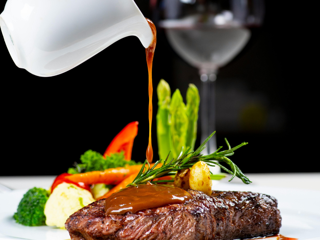 A gourmet steak topped with rich sauce, accompanied by colorful vegetables and garnished with rosemary