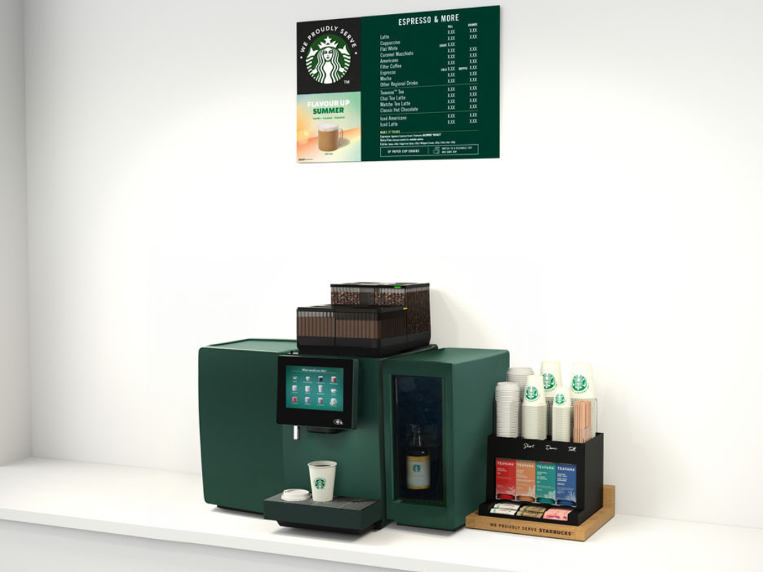 Starbucks self-service coffee station with a green coffee machine, disposable cups, stirrers, and a menu board on a white cou