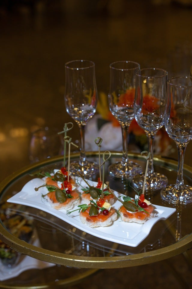 Elegant smoked salmon canapés with capers and red garnish, served on a white plate with empty champagne glasses