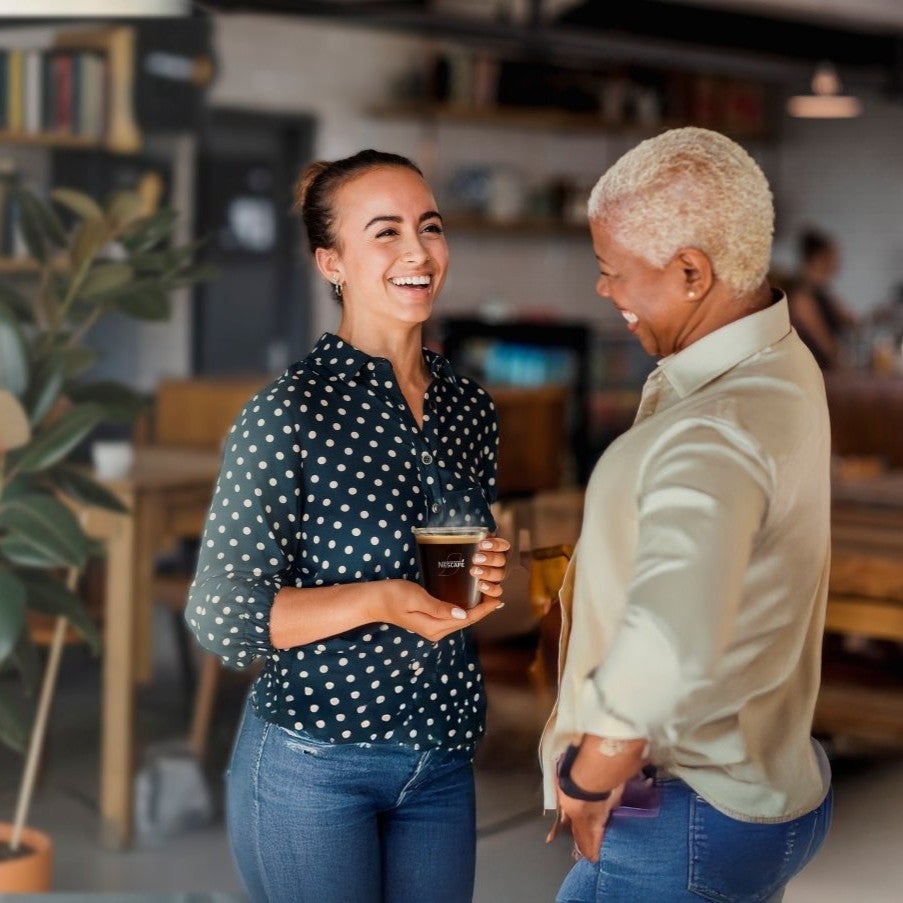 two women holding nescafe coffee and smiling