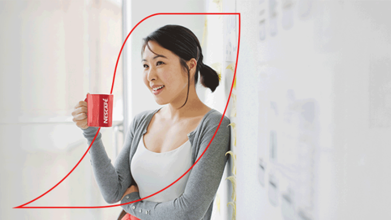 Female leaning back against a wall enjoying a mug of Nescafe coffee