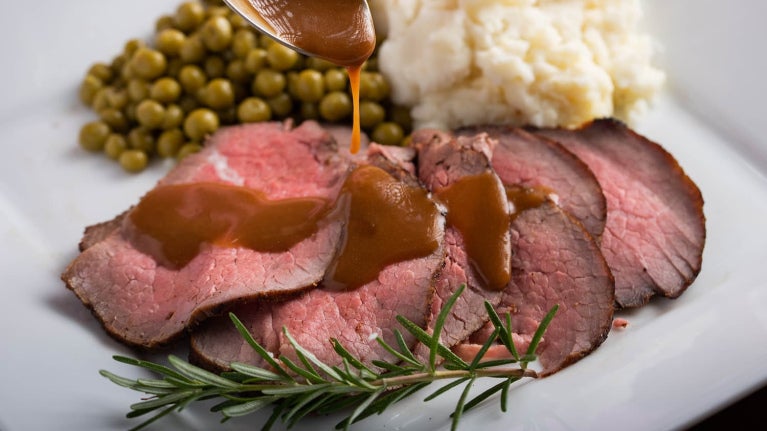 Gravy poured on roast beef with potatoes and peas.