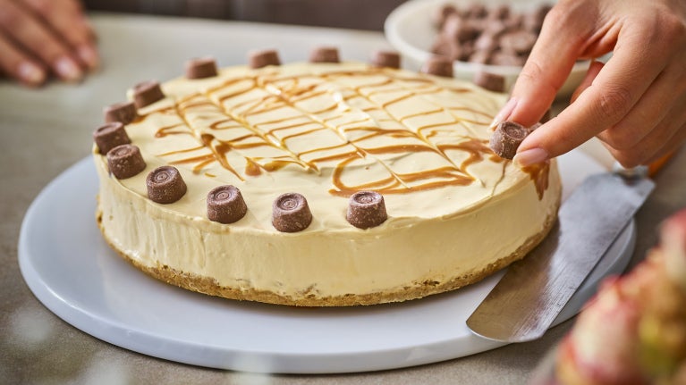 hand placing rolo pieces on cheesecake 