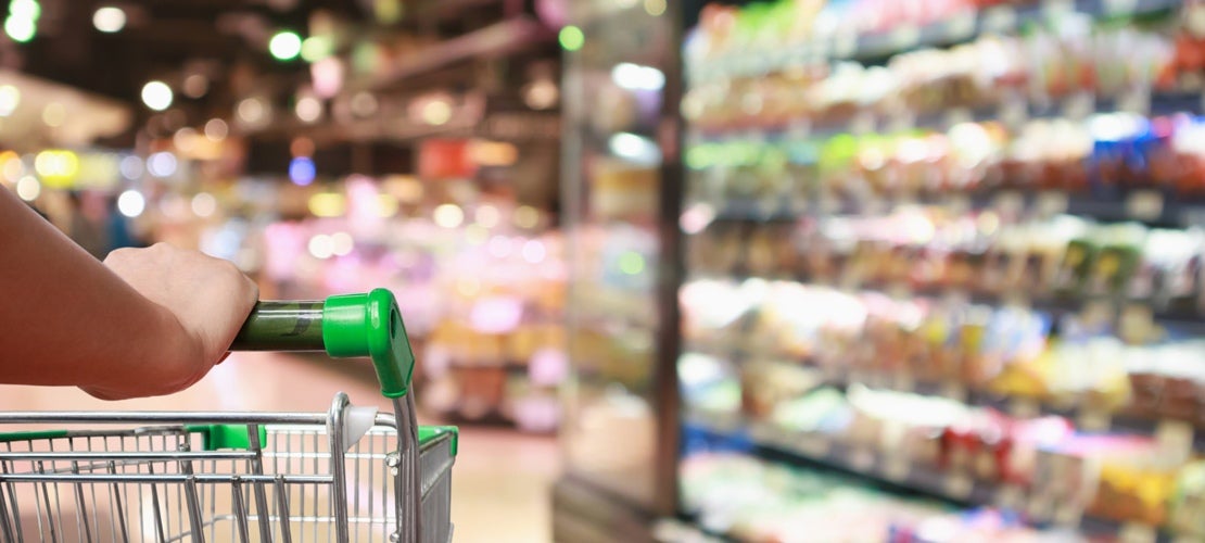 Hand holding trolley at supermarket with blurred view of the shelves full of packaged products