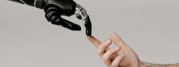 A human hand touching the finger of a robot’s hand.