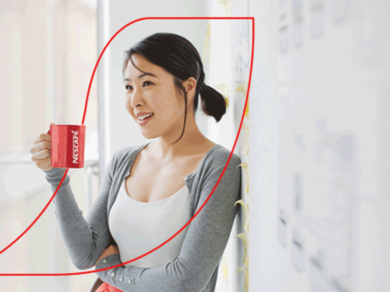 Female leaning back against a wall enjoying a mug of Nescafe coffee