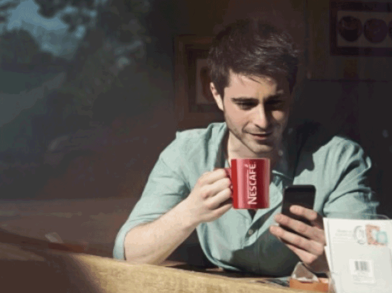 Males sitting enjoying a mug of Nescafe coffee looking at his phone