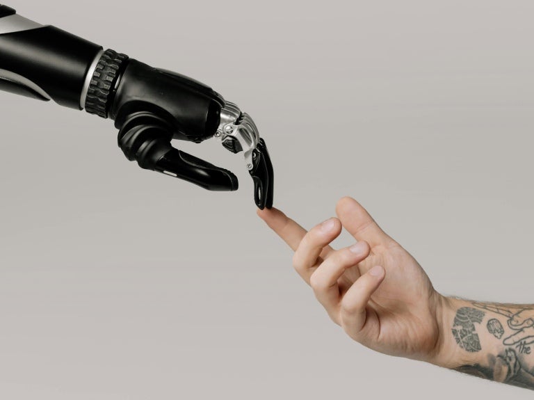 A human hand touching the finger of a robot’s hand.