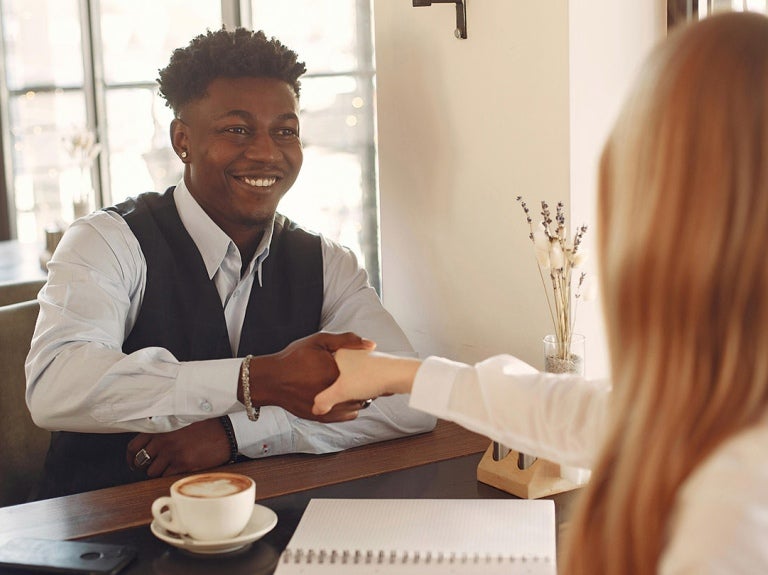 an interviewee sat at a table, smiling whilst shaking hands with an interviewer