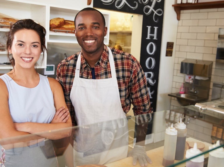 a male and female small business owners behind a bakery counter, smiling