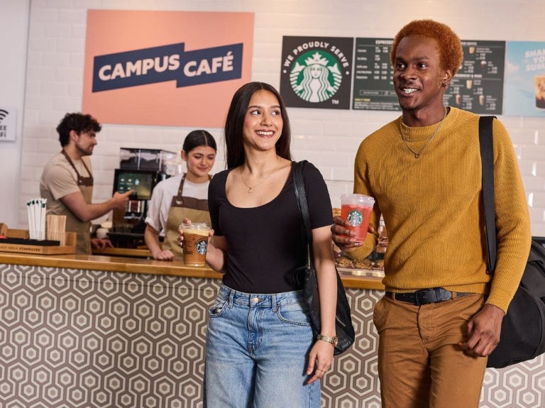 two students holding coffee cups at university cafe