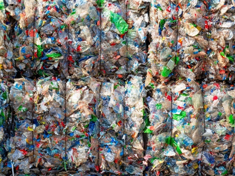 A close-up of compacted plastic waste, showing a colorful mix of crumpled bottles and wrappers, highlighting recycling