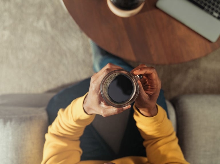hand holding a mug of black coffee at a desk