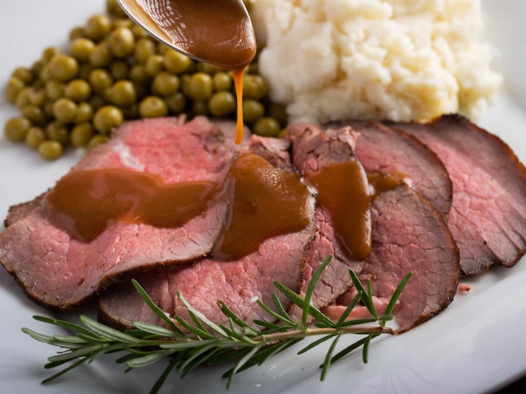 Gravy poured on roast beef with potatoes and peas.