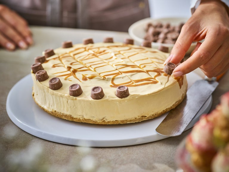 hand placing rolo pieces on cheesecake