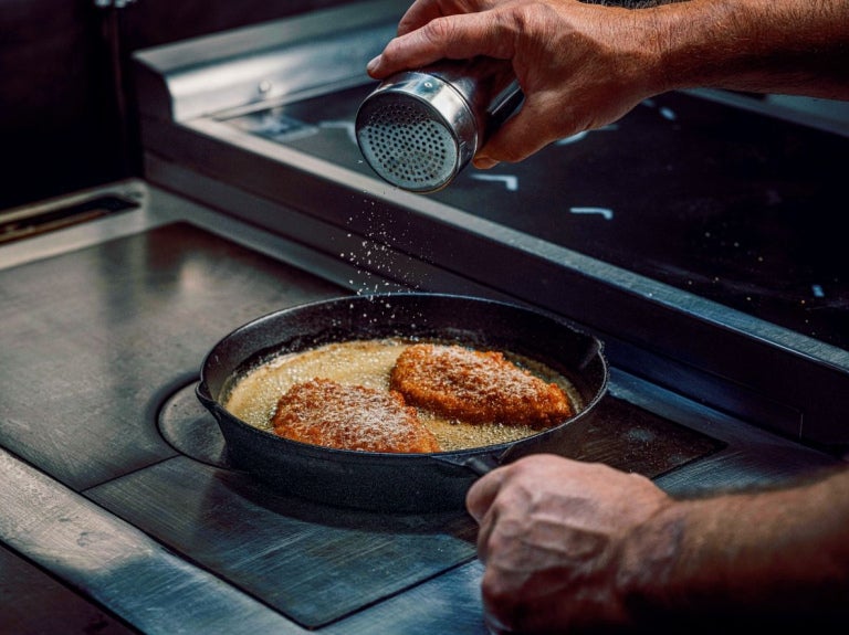 chef shaking truffle seasoning into chicken dish