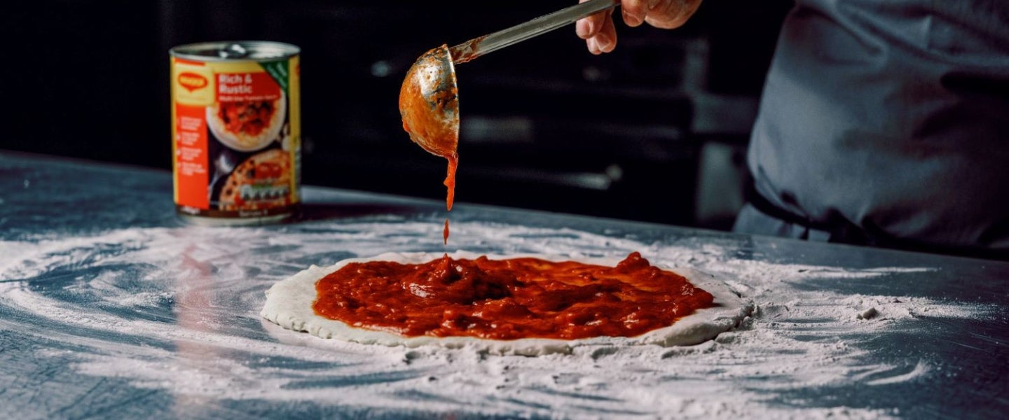 maggi rich and rustic sauce being spread on pizza