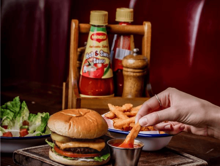 Burger &amp; fries dish on a pub table with sauces in the background