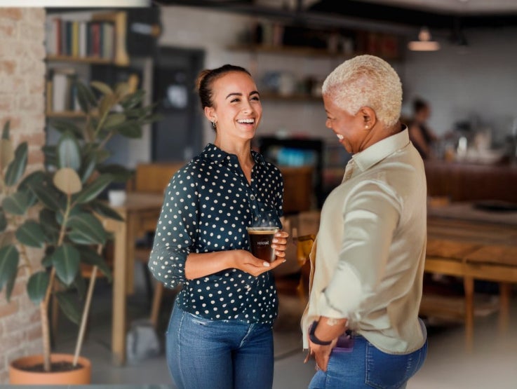 two women smiling and holding a coffee