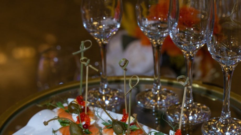 Elegant smoked salmon canapés with capers and red garnish, served on a white plate with empty champagne glasses