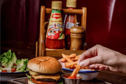 Burger &amp; fries dish on a pub table with sauces in the background