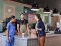 Two women and a barista at a café counter, with one woman wearing scrubs and the other taking a Starbucks drink.