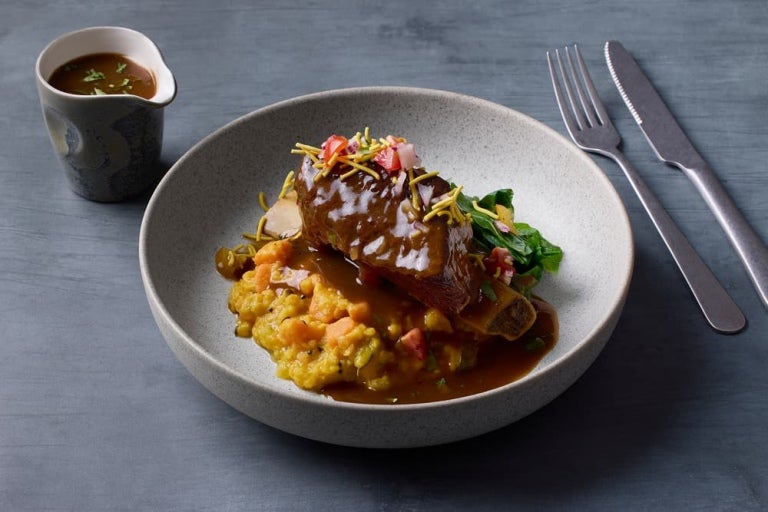 A plated dish featuring tender meat topped with sauce, garnished with vegetables and herbs