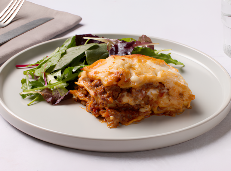 Slice of lasagna with melted cheese and ground meat served with a side of mixed green salad on a white plate.