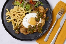 Milanesa a Caballo with Chimichurri Rojo and chips on a black plate