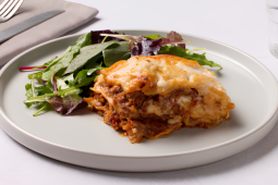 Slice of lasagna with melted cheese and ground meat served with a side of mixed green salad on a white plate.