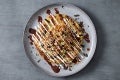 A beautifully arranged okonomiyaki topped with drizzles of sauce, mayonnaise, green onions on a gray plate.