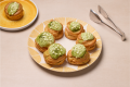 Plate of six cream puffs topped with green matcha glaze and white chocolate chips, with tongs and an additional puff