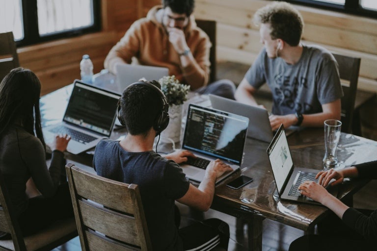 A group of people working on laptops, sat around a table.