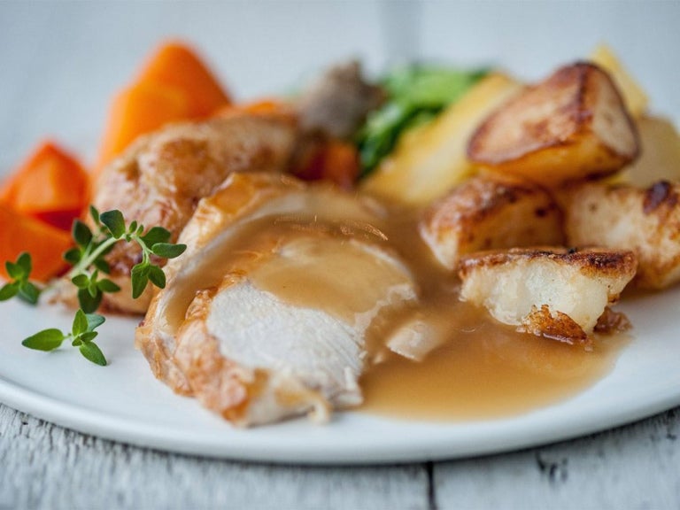 A plate featuring sliced roasted chicken with gravy, golden roasted potatoes, vibrant carrots, and a sprinkle of herbs.