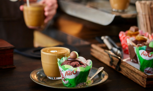 Cup of latte and chocolate cupcake topped with a chocolate ball on a plate with a small fork, on a dark wooden table.